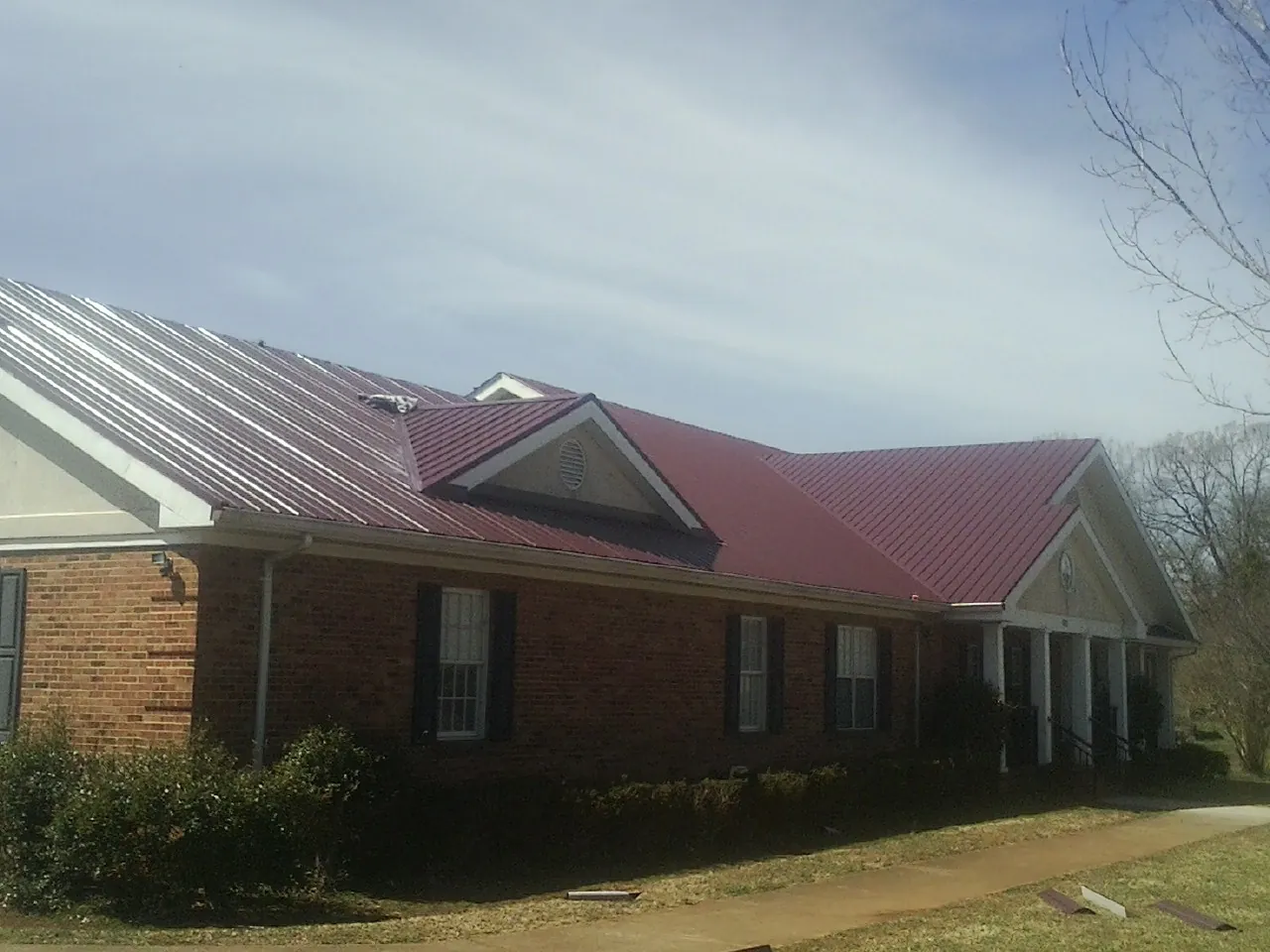 Red metal roof with gabled entries on a long brick building, from a Hail Damage Roof Repair job in Mystic