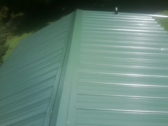 New green metal panels meeting at the ridge of a roof — Flat Roof Repair work by our crew in Mystic