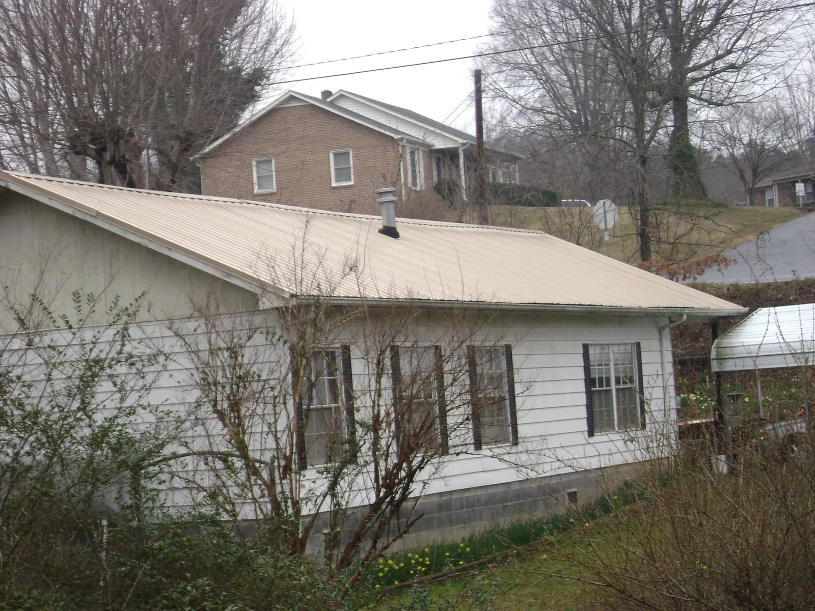 Tan metal roof on a white sided house set into a hillside — Commercial Roofing by Roofing Brothers in Mystic