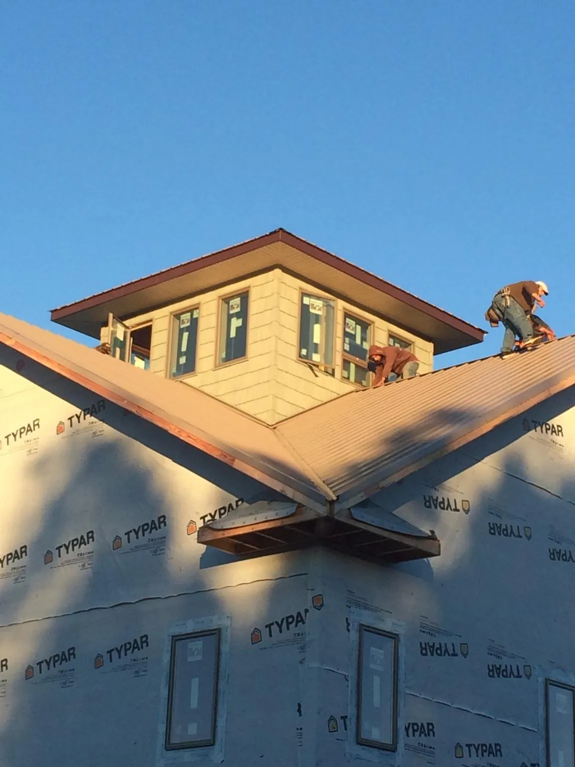 Roofers working around a rooftop cupola on a new metal roof at sunset — Roof Waterproofing in Mystic by Roofing Brothers